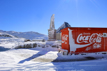 A statue of Sainta Margarita and a stall selling soft drinks stand together at the snow covered summit of the St. Gotthard Pass (2,106 m).