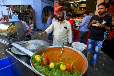 The owner of a stall selling a spicy curry fries an accompanying snack.