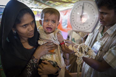 Community volunteer, Mohammed Younuse Zan Mal Lida with her daughter, one year old Remus, who has been ill for days and was brought in to the health centre at the Hakinpara Rohingya refugee camp where...