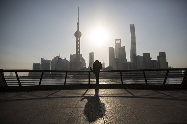 A man exercises on the Bund while in the background the sun rises behind buildings of Pudong's Lujiazui financial district across the Huangpu River.