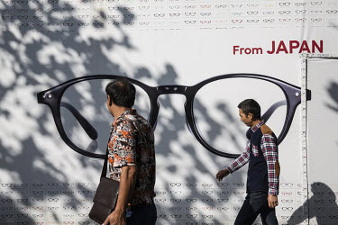 Pedestrians walk past a shop advertising its Japanese eye wear.