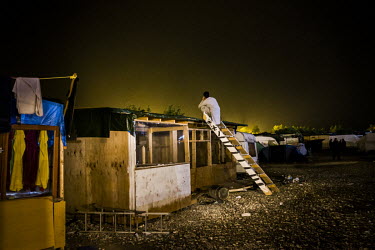 A man stands on a ladder while seeking a better signal for a mobile phone call in the so-called 'Jungle' refugee camp. The police had recently visited the premises to warn the owner not to build the p...