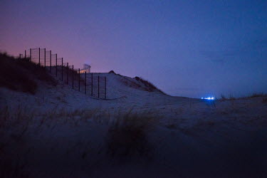 The lights from a patrolling police vehicle appear on a beach near the so-called 'Jungle' refugee camp. Refugees from the camp have no more than four minutes to run one kilometre along the beach, get...
