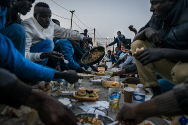 A group of refugees from Sudan, Eritrea and Ethiopia eating breakfast during Ramadan while sitting in the open air mosque in the so-called 'Jungle' refugee camp.