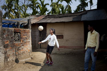 Binita Tanti (15), a member of Smriti Adolescent Girls Group on the Rupai Tea Estate and a keen football player, practices outside her family home while her father, Bhokkhor Dhan Tanti, watches.