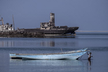 A fisherman pulls his boat through shallow water, past the wrecks of cargo ships of the coast at Berbera.