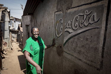 A woman stands beside an old Coca-Cola advertisement painted on the wall of a building in Korogocho.