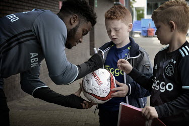 A player from the AFC Ajax football club's second team adds his autograph to a young fan's ball.