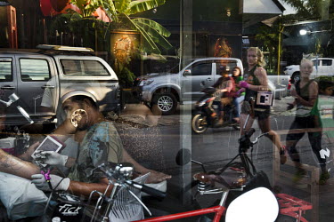 Two western women out jogging are reflected in the glass of a tattooist parlour.