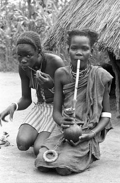 Two Anuak girls, one of whom smokes a pipe made from a gourd.