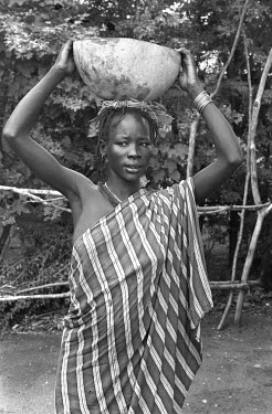 An Anuak woman carries a gourd on her head.