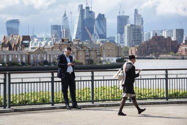 A businessman and woman looking at their mobile phones with the River Thames and the City of London in the background.