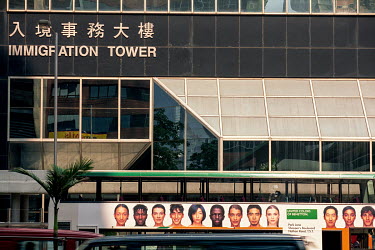 A bus with a Beneton advertisement on its side showing multi-ethnic faces passes Hong Kong's Immigration Tower building.