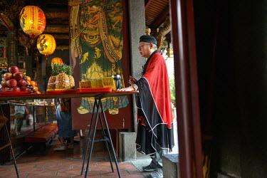 A Taoist priest stands beside a table holding various offerings at the Bao An Temple. The temple was constructed in 1742 and inducted into UNESCO for cultural heritage conservation in 2003.