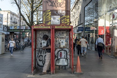 A man counts his money while standing in a phone booth in Brixton.