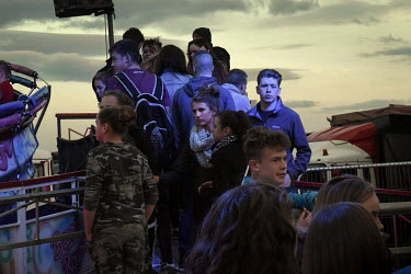 Teenagers queue for rides at a travelling fairground.