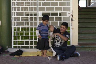 Wilmer Espino (13) bandages the cast covering the left arm of his younger brother Angel Espino (4) as they sit outside the Office for Assistance to Migrants. Both children, undocumented migrants origi...