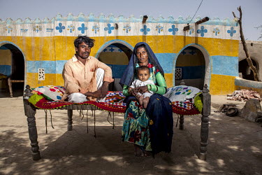 Haryoo and Tarjan, holding their son Peeriyo, 8 months, on a day bed in front of their house.