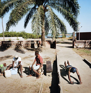 A man exercises in front of his house while two friends clean fish for their lunch.