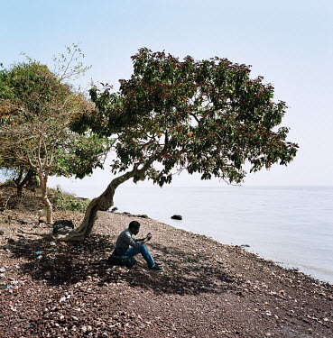 A man wait sitting in the shadow of a tree.