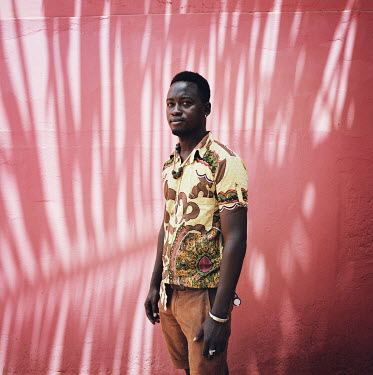 Janito (24) stands by a red wall in the yard of his house.