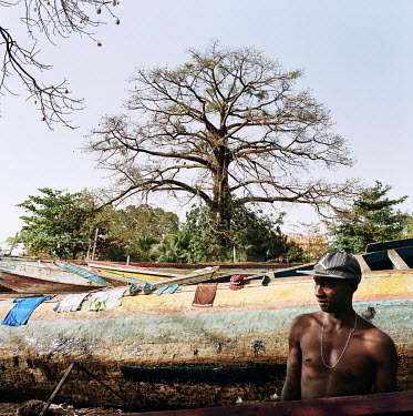 A man standing between beached pirogues waiting for his clothes to dry.