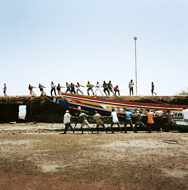 People struggle to move a fishing boat into the water at low tide.