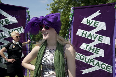 A woman stands beside a banner (in the Suffragist colours 'Purple, White and Green') with the slogan 'We Have The Courage' as she prepares to take part in 'Processions', a mass participation artwork,...