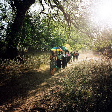 A group of women from a neighbouring village walk in file along a path as they arrive for a celebration in the village of Susana.
