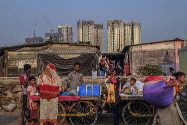 A man selling snacks from a mobile stall beside an area of low-rise slum housing is in stark contrast to the skyscrapers of a residential development rising behind them.