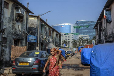 A woman walks along a street strewn with rubbish and lined with dirty low rise buildings while in the background the steel and glass IL&FS Financial Centre and Deutsche Bank buildings in Bandra East s...