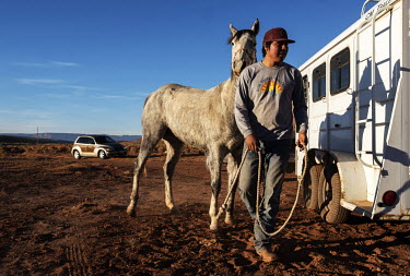 A Native American returns his horse to a trailer after a training session roping horses.