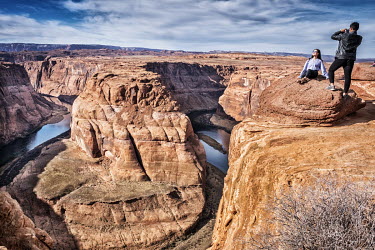 Asian tourists posing for photographs on the cliff edge at Horseshoe Bend, an incised meander on the Colorado River.