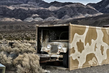 A camouflaged jeep in a camouflaged container in the desert.