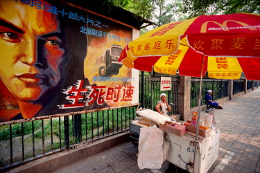 A woman selling snacks from a street stall set up beside a billboard advertising the Hollywood movie 'Speed', and picturing its star Keanu Reeves.