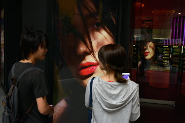 A couple stand beside an advert which is also reflected in shop window in the Ximending district.