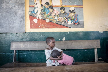 Malnourished children sit below a a picture, in a health centre, depicting a group of children eating a meal.