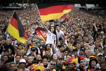 Fans wave the national flag as a crowd watches Germany play Sweden at the FIFA 2018 World Cup on a giant screen erected on the Fanmeile (fan mile), Strasse des 17. Juni.
