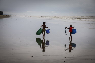 Ajij and Akhi, the sons of a fisherman, carry plastic containers acrcoss the beach while they wait for their father to return from a fishing trip. Children often accompany their fathers and learn skil...