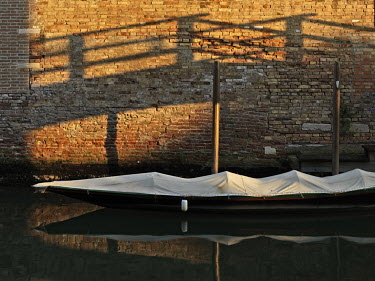 The shadow of a bridge falls on a wall near a moored gondola.