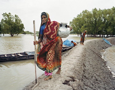 Fatema and Mojida walk along a dike, carrying drinking water from a well back to their village. As sea levels rise as a result of climate change, drinking water is becoming more salinated and increasi...