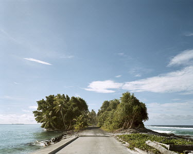 A road traverses one of the narrowest parts of Funafuti Atoll. The atoll's landmass is a mere 2.4 square kilometres, encircling a lagoon 18 kilometres long and 14 kilometres wide. Over half the popula...