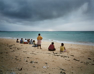 Women watch fishermen who are taking the risk of going out to fish from the beach as a storm approaches.