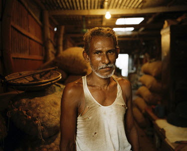A man stands in a warehouse stocked with bags of onions, rice and other food stuffs.