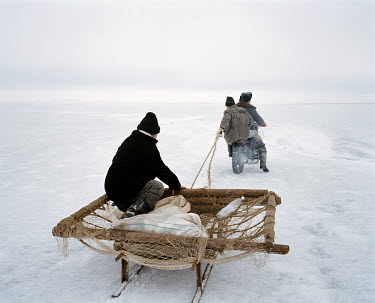 A motorcycle's pillion passenger pulls a man on a sled across the frozen Aral Sea.