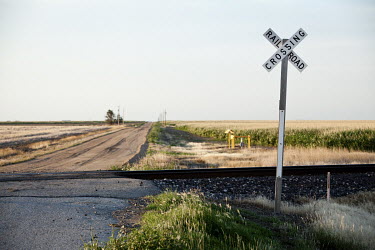 A rail crossing on a dirt road that cuts across corn fields and the prairie.