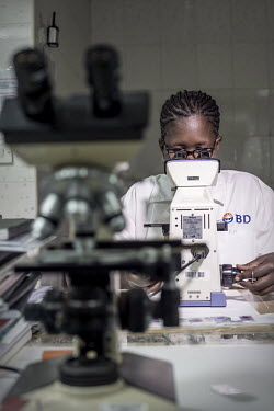 A woman examines a blood slide sample while testing for malaria.