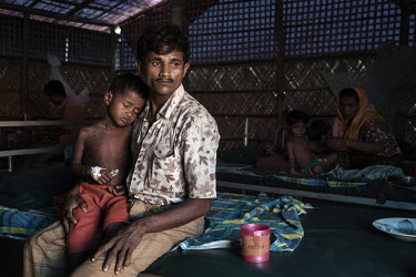 Rohingya refugee, Noor Kodor (4), who is suffering with measles and pneumonia, is comforted by his father in the measles isolation ward of the MSF Kutapalong Clinic.