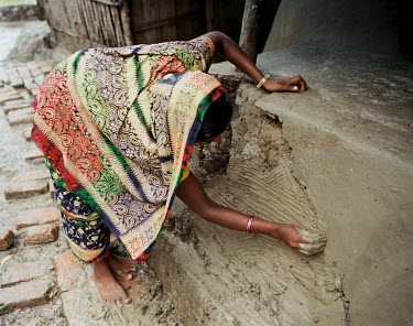 A woman re-plasters her home. During the monsoon, houses built of mud tend to disintergrate and must constantly be repaired.