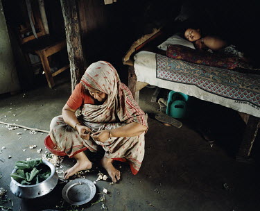 A woman prepares vegetables while her son sleeps beside her.
